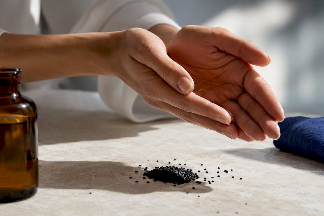 Hands warming black seed oil near black seeds