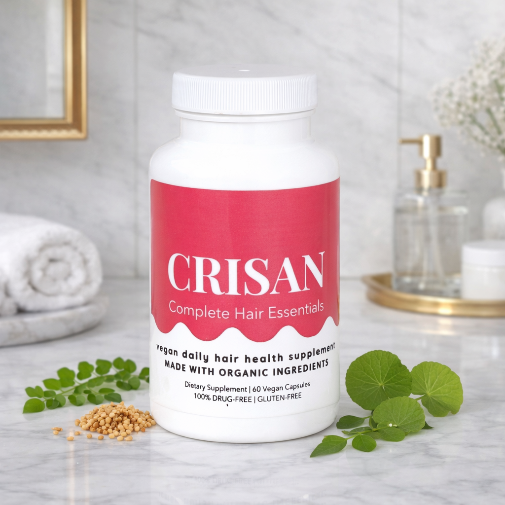 Supplement bottle labeled 'CRISAN Complete Hair Essentials' on a bathroom counter with green leaves and a towel in the background.